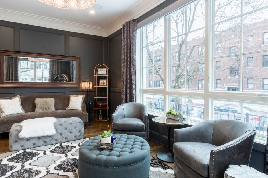 A living room featuring dark grey painted walls with decorative paneling and a large, rectangular mirror framed in wood hanging above a plush, dark grey sofa adorned with several cushions and a white 