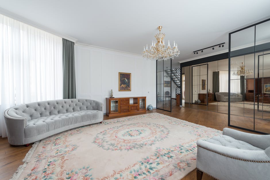 A living room featuring dark grey painted walls with decorative paneling and a large, rectangular mirror framed in wood hanging above a plush, dark grey sofa adorned with several cushions and a white 